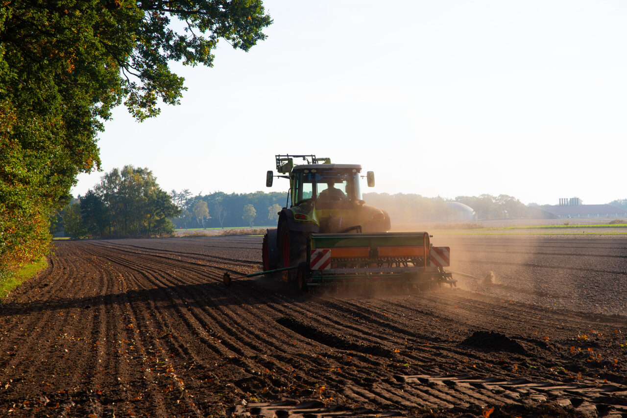 Ein Landwirt eggt mithilfe eines Traktors ein Feld.